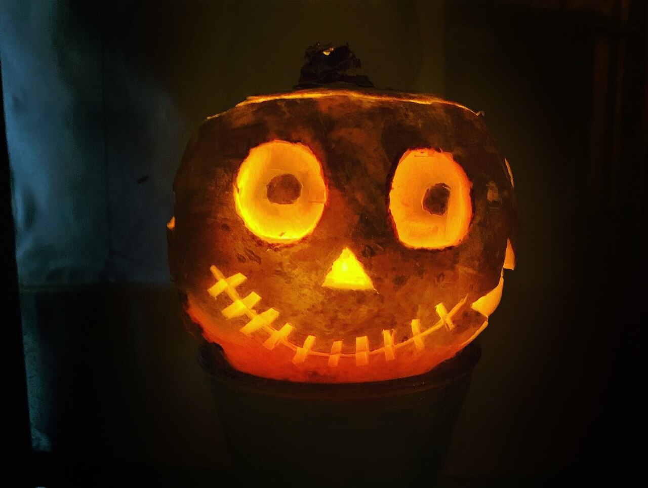 A carved turnip lantern glowing in the dark with round eyes and a jagged grin